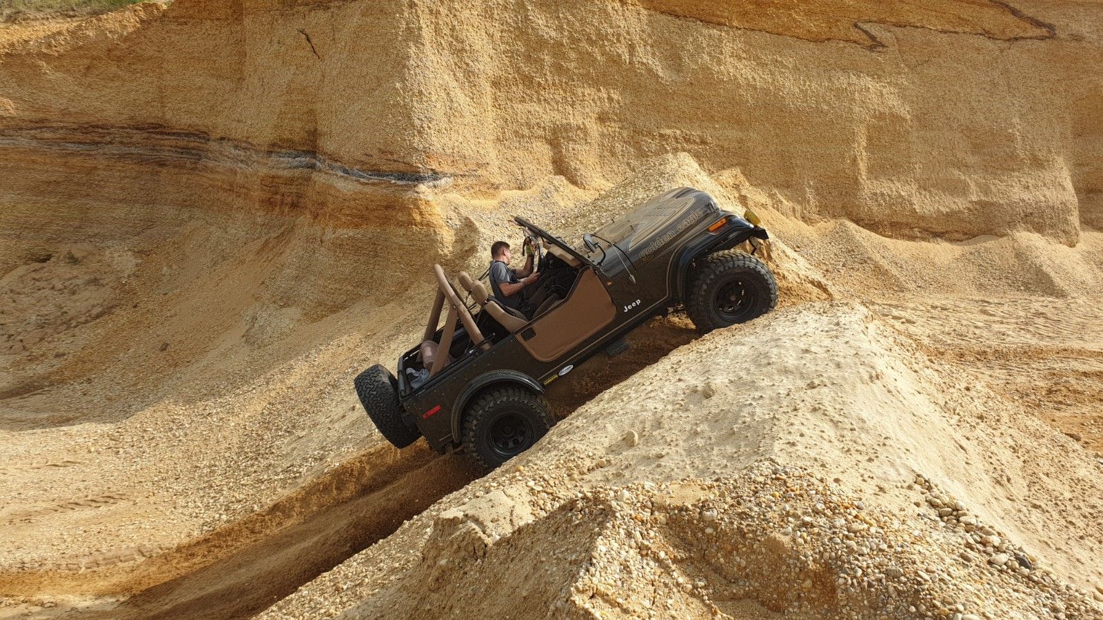 Geländewagen fährt steil einen sandigen Hügel vor einer Felswand hinauf