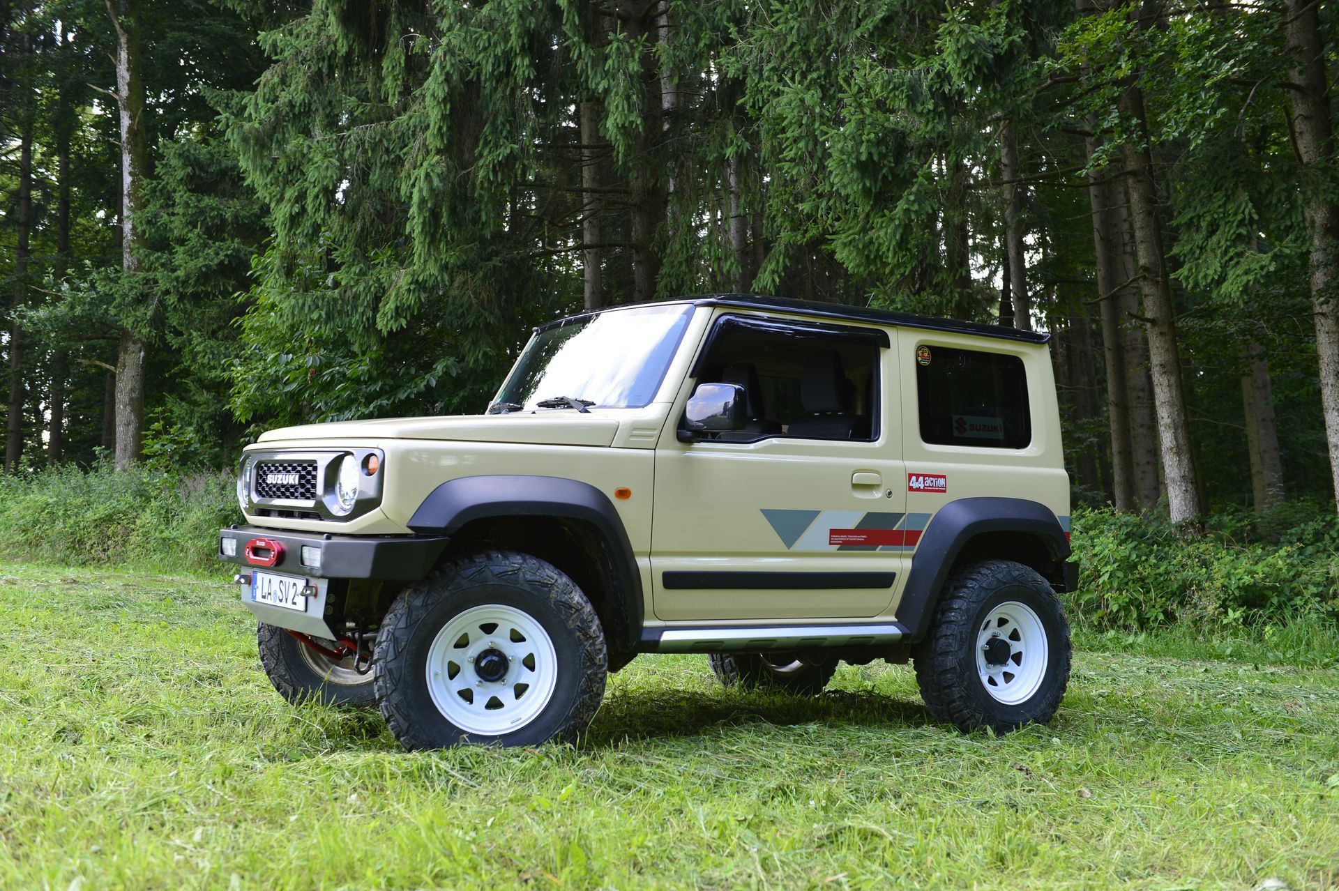 Geländewagen mit kurzem Radstand und weißen Felgen steht auf Gras vor Nadelwald