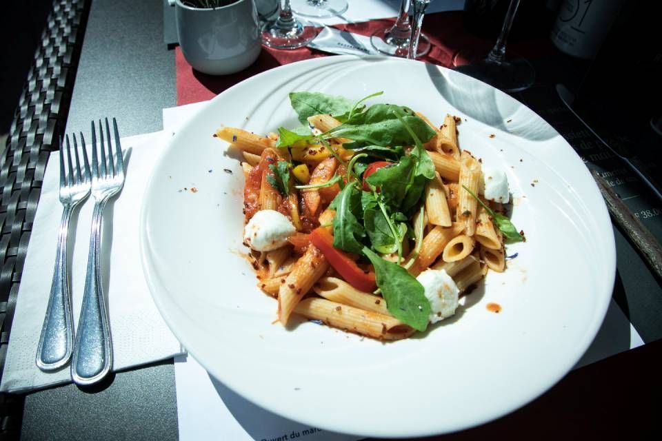 Salade de pâtes avec de la verdure sur une assiette blanche, à côté de fourchettes sur une table de restaurant