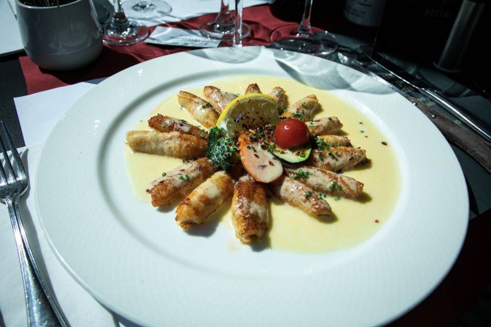Assiette de fruits de mer gastronomique avec sauce, herbes et tomate cerise, présentée sur une table blanche.