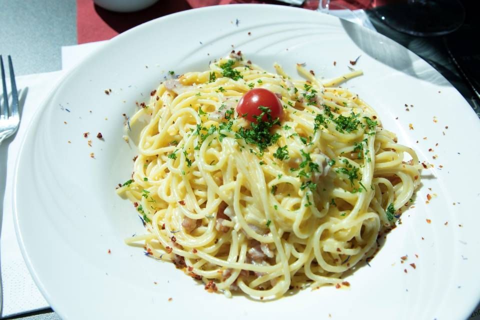 Assiette de spaghettis aux herbes et à une tomate cerise, servie dans un plat blanc sur une table.