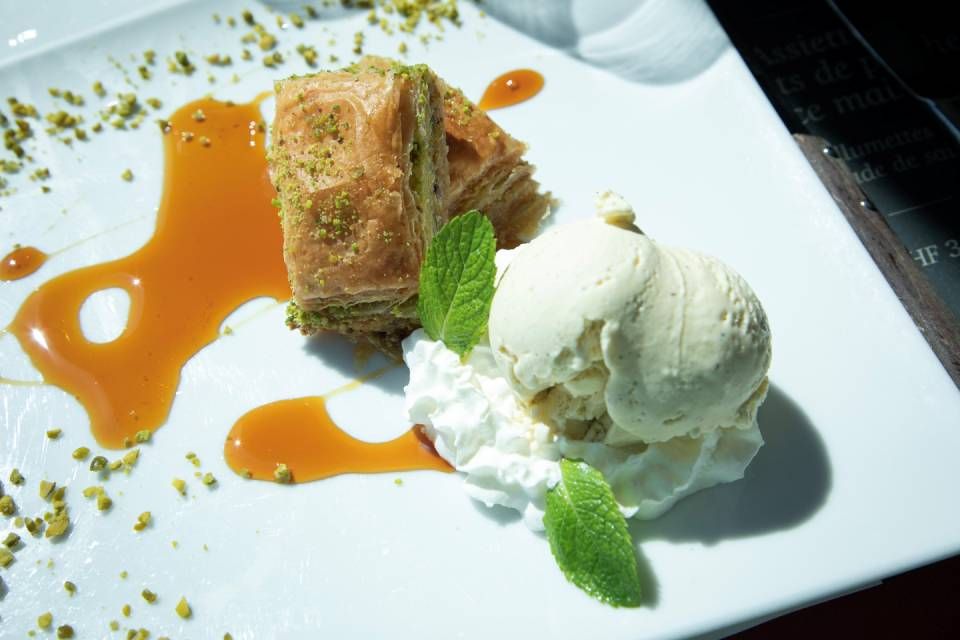 Assiette de dessert composée de glace à la vanille, de pâtisserie et de sauce à l'orange sur un plat blanc, garnie de menthe.