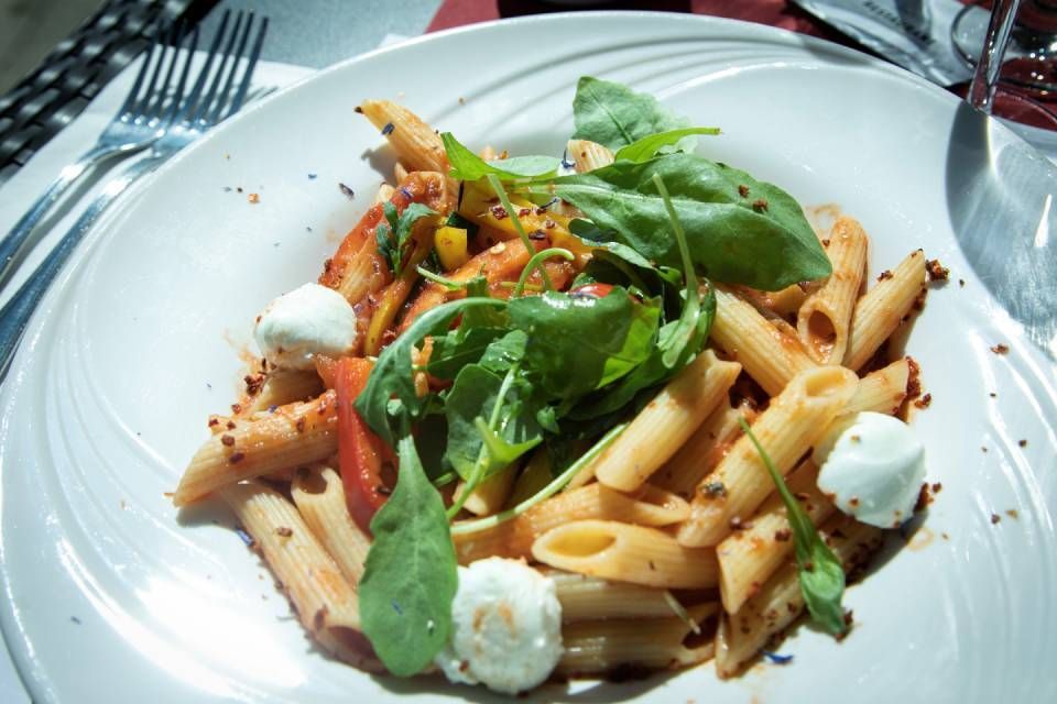 Pâtes penne aux légumes verts et quenelles de fromage blanc sur une assiette blanche