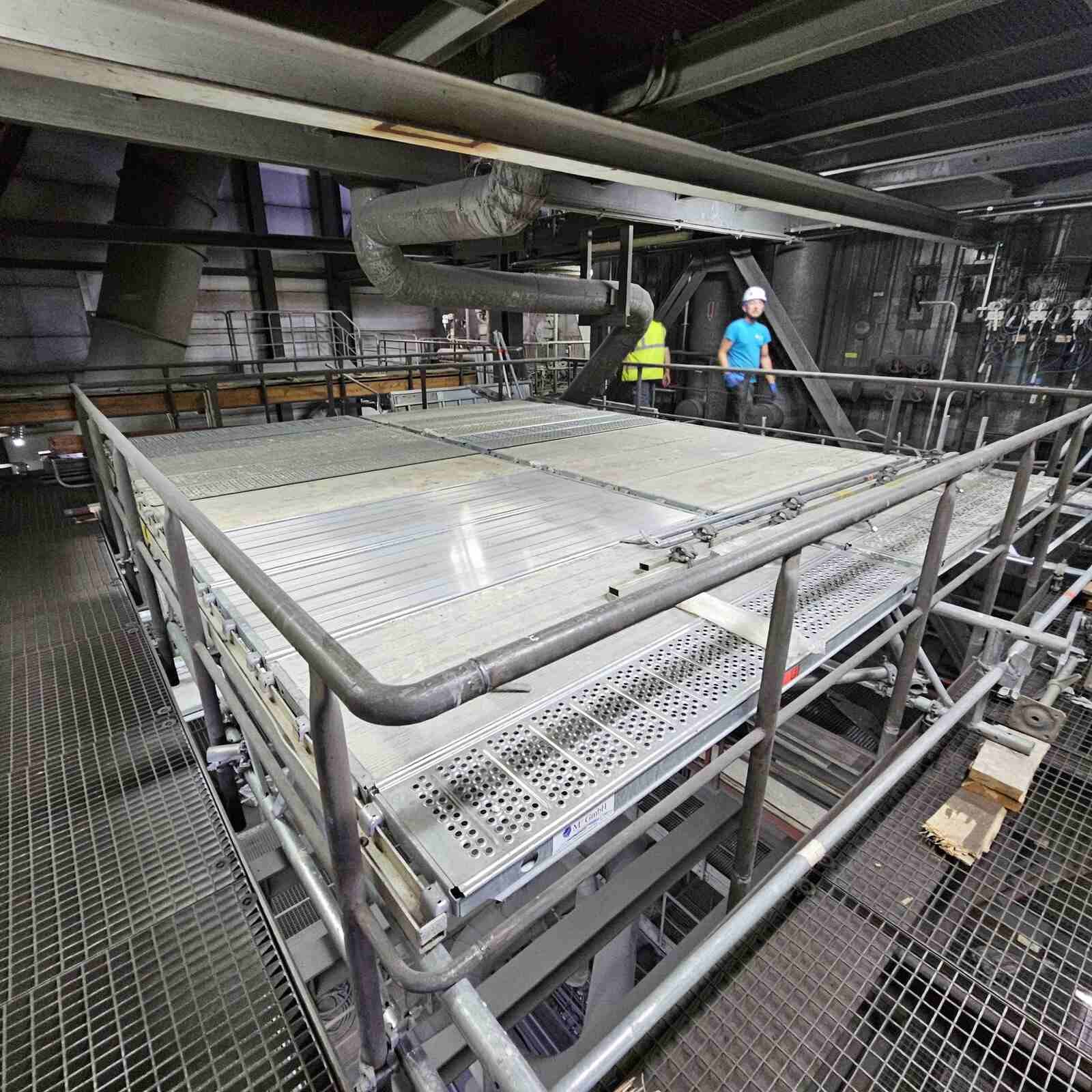 Zwei Männer stehen auf einer Metallplattform in einer Fabrik.
