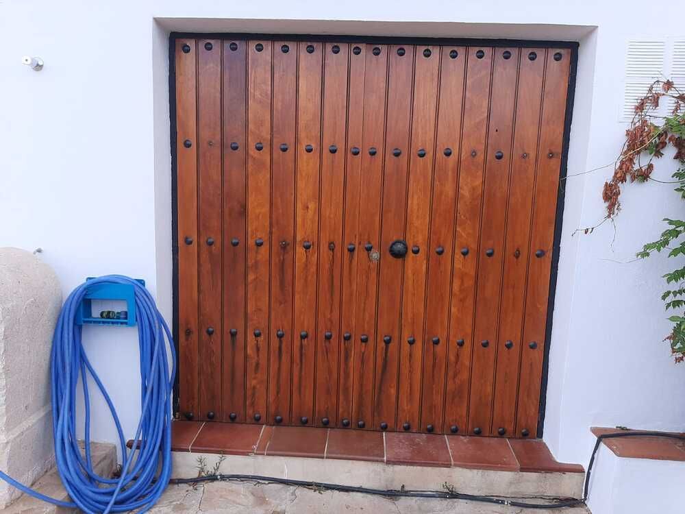 Puerta de madera con detalles de metal, colocada en una pared blanca con una manguera azul enrollada.