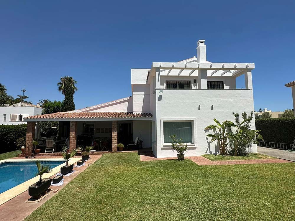 Casa blanca con piscina y césped verde en un día soleado.