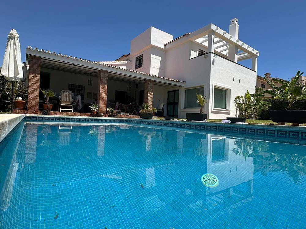 Casa blanca con piscina al frente, bajo un cielo azul claro.