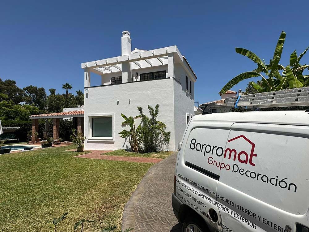 Casa blanca siendo pintada, con una furgoneta aparcada en primer plano en la que se puede leer 