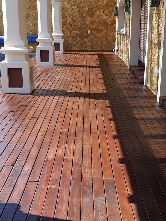 Terraza de madera con tablones de color marrón oscuro, pilares y una pared de piedra al fondo.