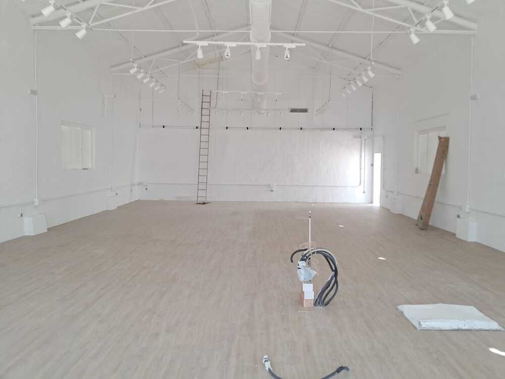 Interior vacío, pintado de blanco, de una gran habitación. Suelo de madera, vigas vistas, lámparas. Escalera apoyada en la pared.