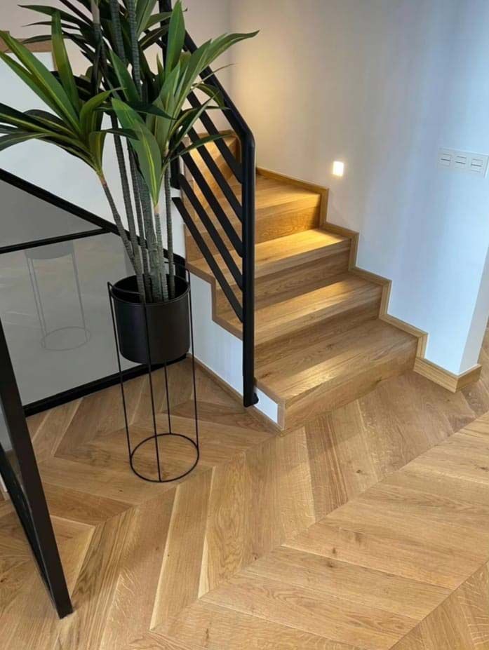 Escalera de madera con barandilla de metal negro y maceta con planta sobre suelo de madera en espiga.