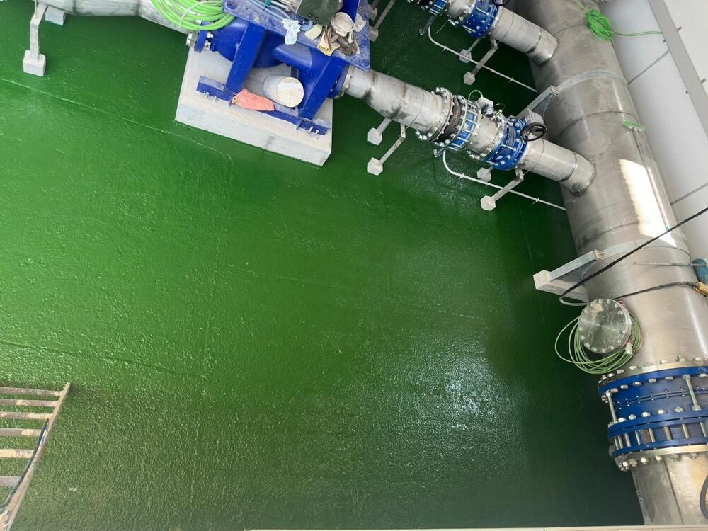 Piso industrial verde con maquinaria azul y tuberías plateadas.