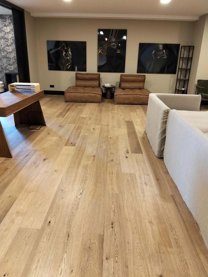 Habitación con suelo de madera, sillas de cuero marrón, obras de arte y sofás blancos.