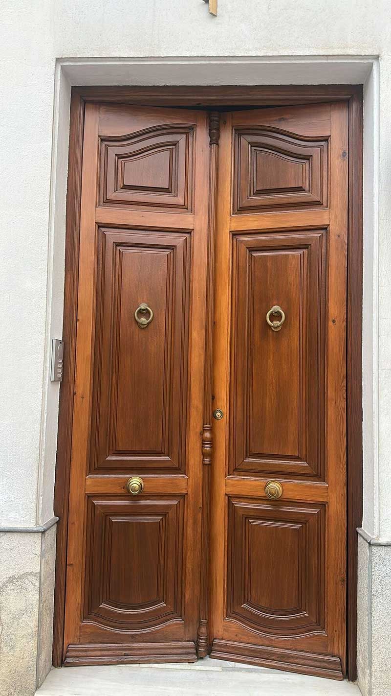 Puertas dobles de madera con herrajes de latón, colocadas en una pared blanca.