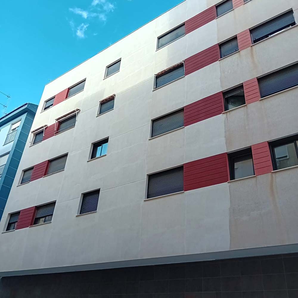 Edificio de apartamentos de varios pisos con fachada blanca y roja contra un cielo azul.