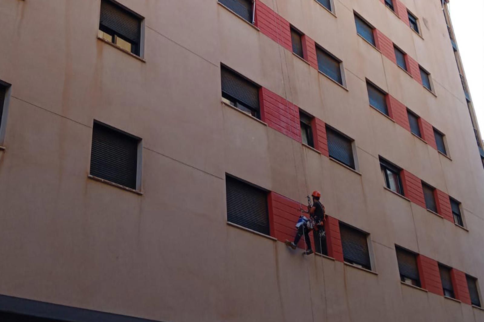 Tres limpiadores de ventanas suspendidos de cuerdas limpiando el exterior de un edificio alto.