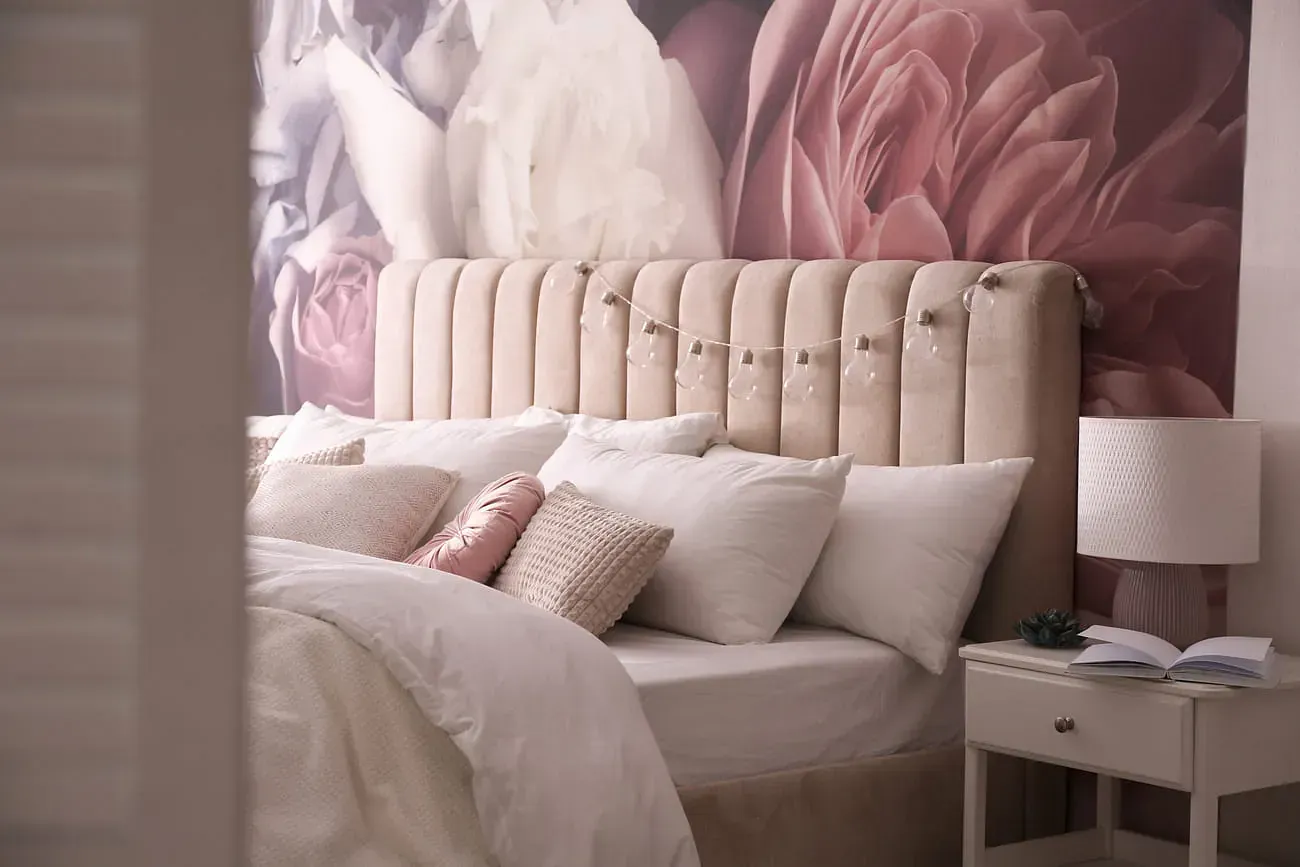 Un dormitorio con una cama, mesita de noche, lámpara y un mural en la pared.