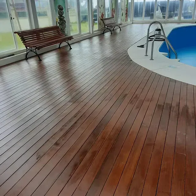 Piso de madera rodea una piscina dentro de un solárium con bancos.
