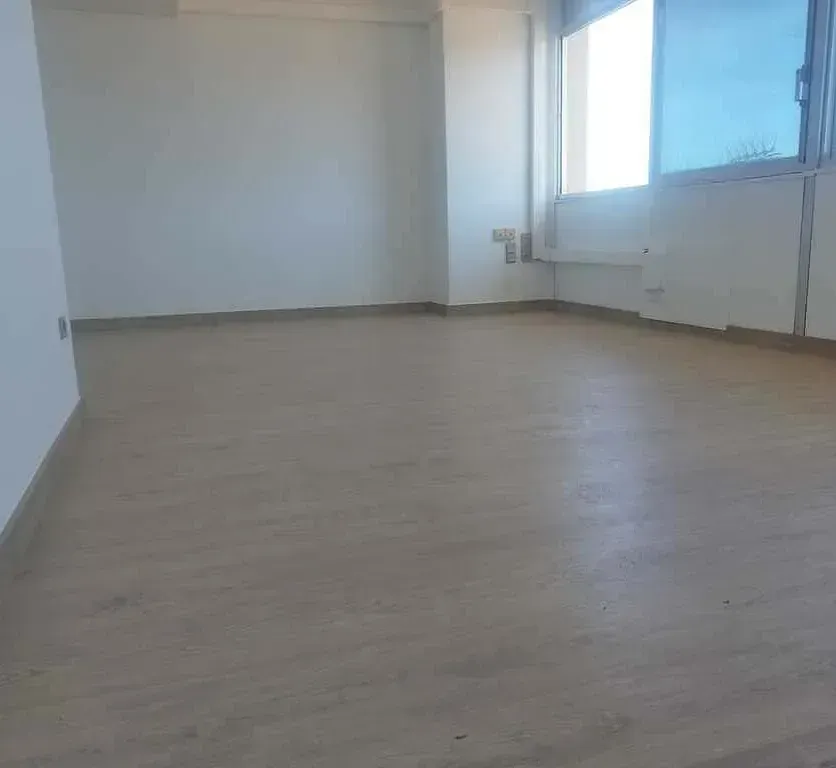 Habitación vacía con suelo de imitación madera clara, paredes blancas y una ventana.