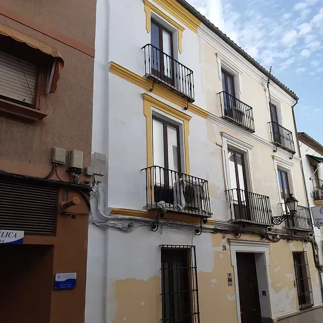 Edificio de tres pisos con fachada blanca y amarilla, pequeños balcones y marcos de puertas y ventanas marrones.