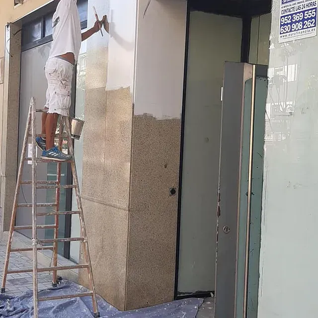 Un hombre está de pie en una escalera pintando un edificio.