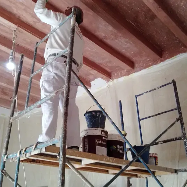 Un hombre pinta un techo de madera sobre un andamio.