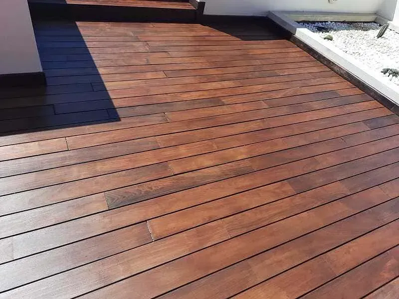 Una terraza de madera con un borde negro se encuentra al lado de un edificio.