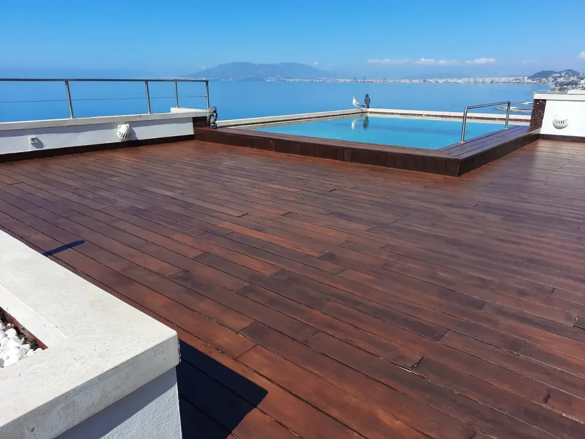 Una terraza de madera con una piscina al fondo.