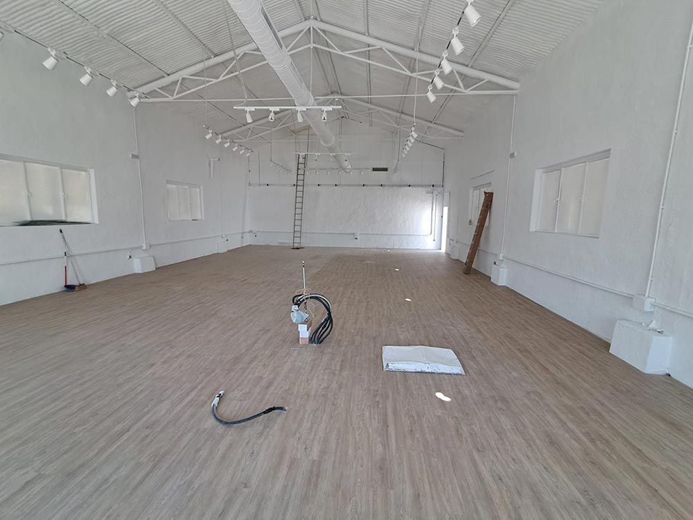 Interior de una habitación vacía con paredes blancas, piso de madera, techo alto y luces en el techo.