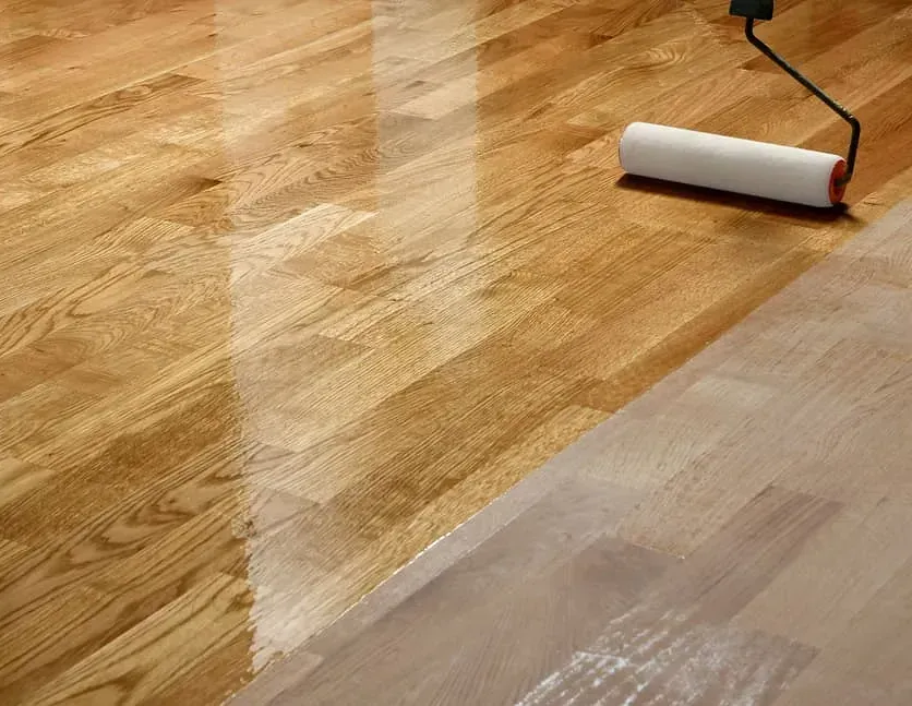 Una persona está pintando un piso de madera con un rodillo.