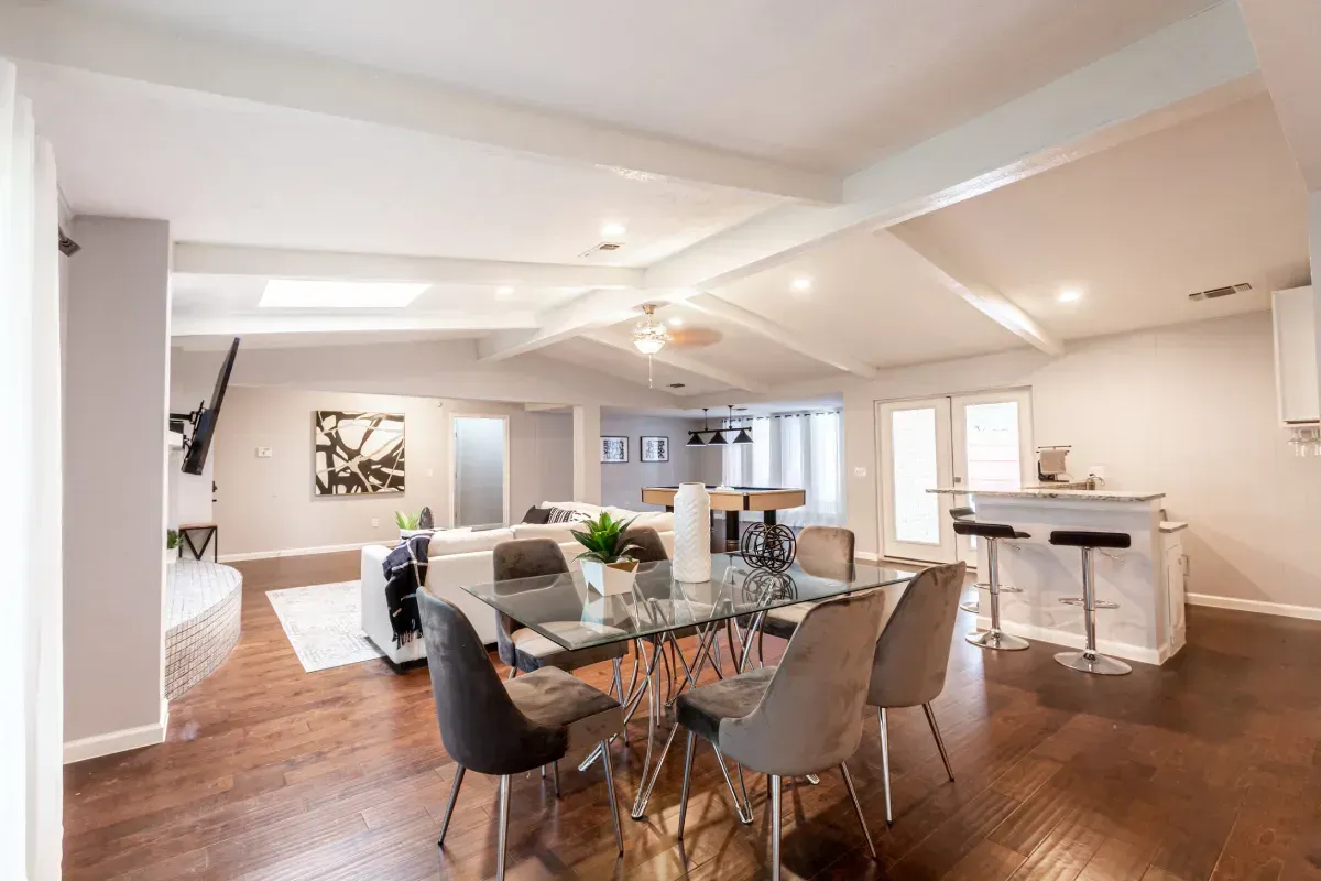 Espacio habitable de concepto abierto con comedor, sala de estar y bar, con pisos de madera y paredes blancas.