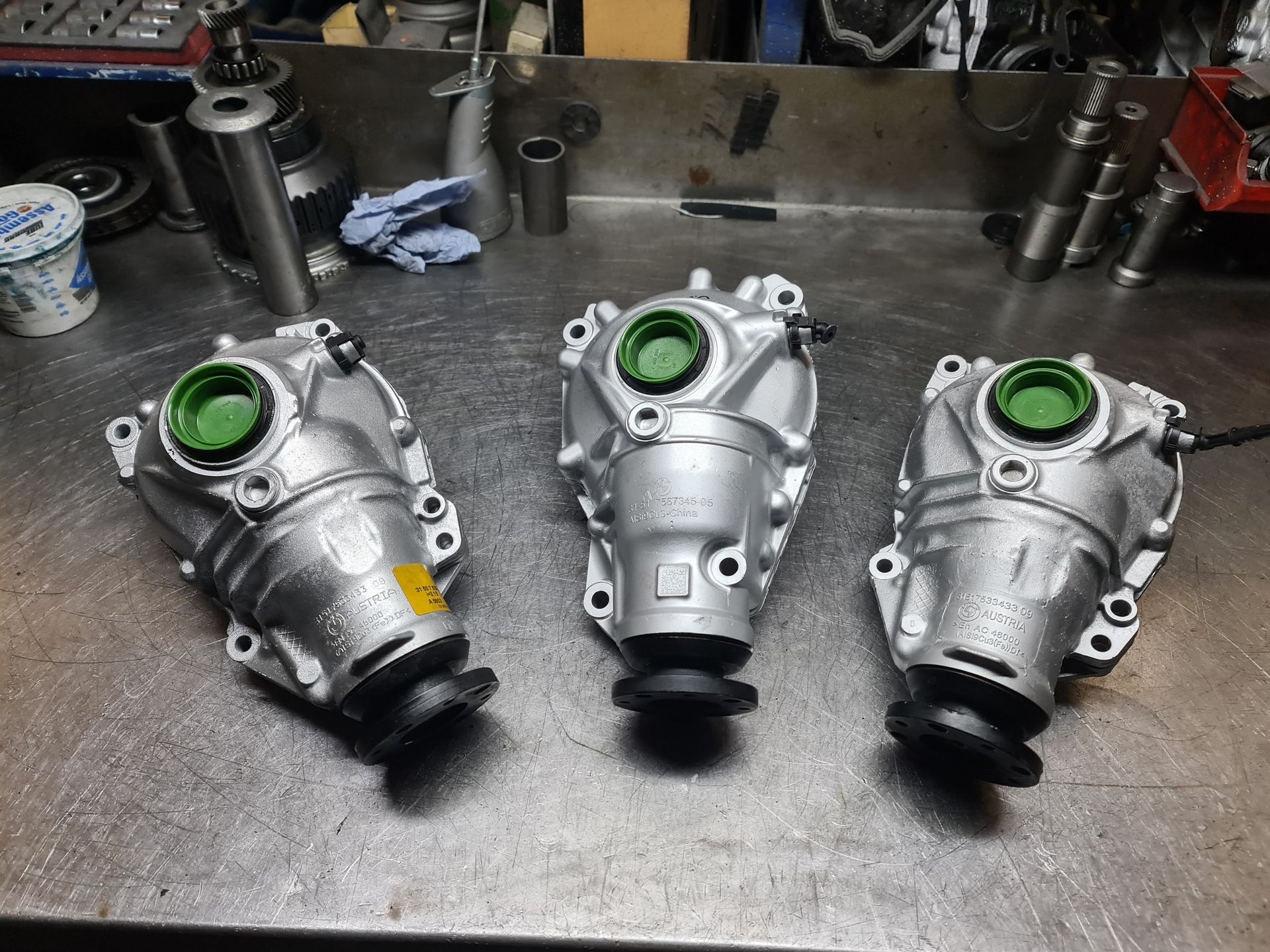 Drei Getriebe liegen auf einem Tisch in einer Garage.
