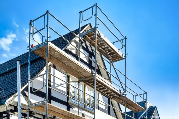 Ein Gerüst umgibt die Giebelfassade eines Fachwerkhauses vor einem klaren blauen Himmel.