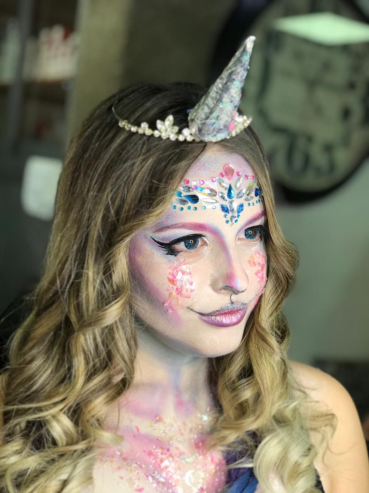 Mujer con pintura facial de unicornio, corona y cabello rubio rizado.