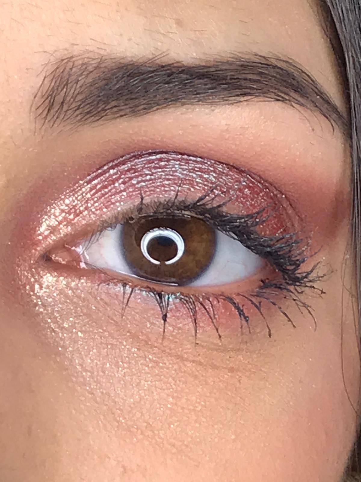 Primer plano de un ojo con sombra de ojos rosa, rímel y ceja marrón oscuro, ojo marrón.