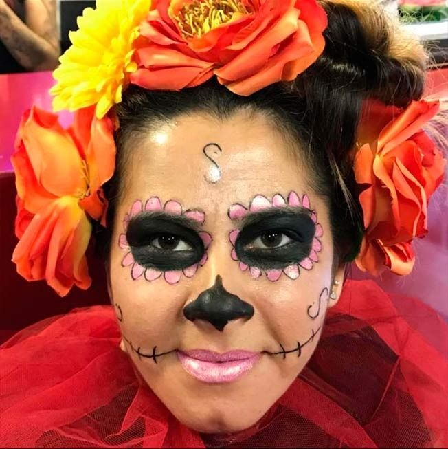 Mujer con maquillaje de Día de Muertos, corona floral, velo rojo.