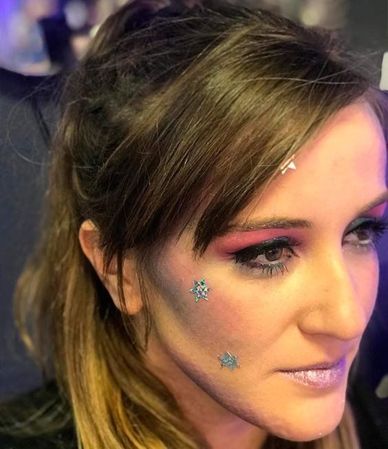 Mujer con maquillaje de galaxia, sombra de ojos rosa, estrellas en la cara y lápiz labial plateado.