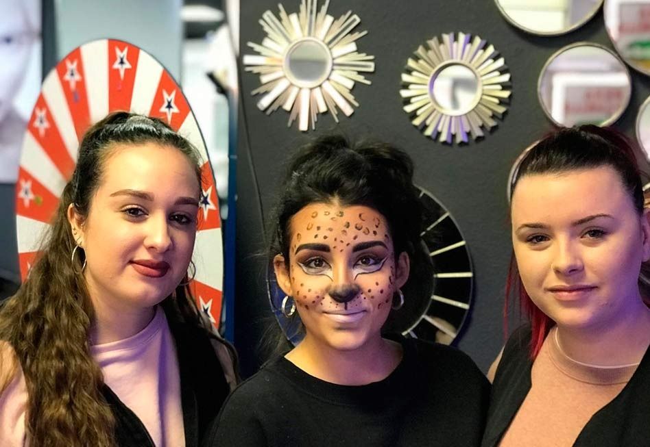 Tres jóvenes posando, una con la cara pintada de guepardo. Escenario negro y rosa.