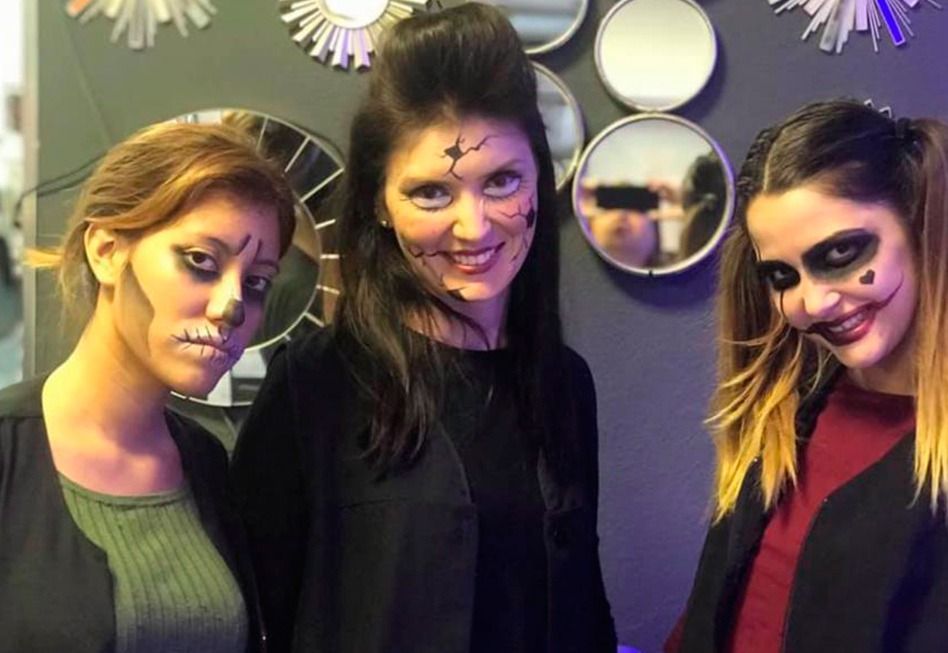 Tres mujeres con disfraces de Halloween y pintura facial aterradora, sonriendo en el interior.