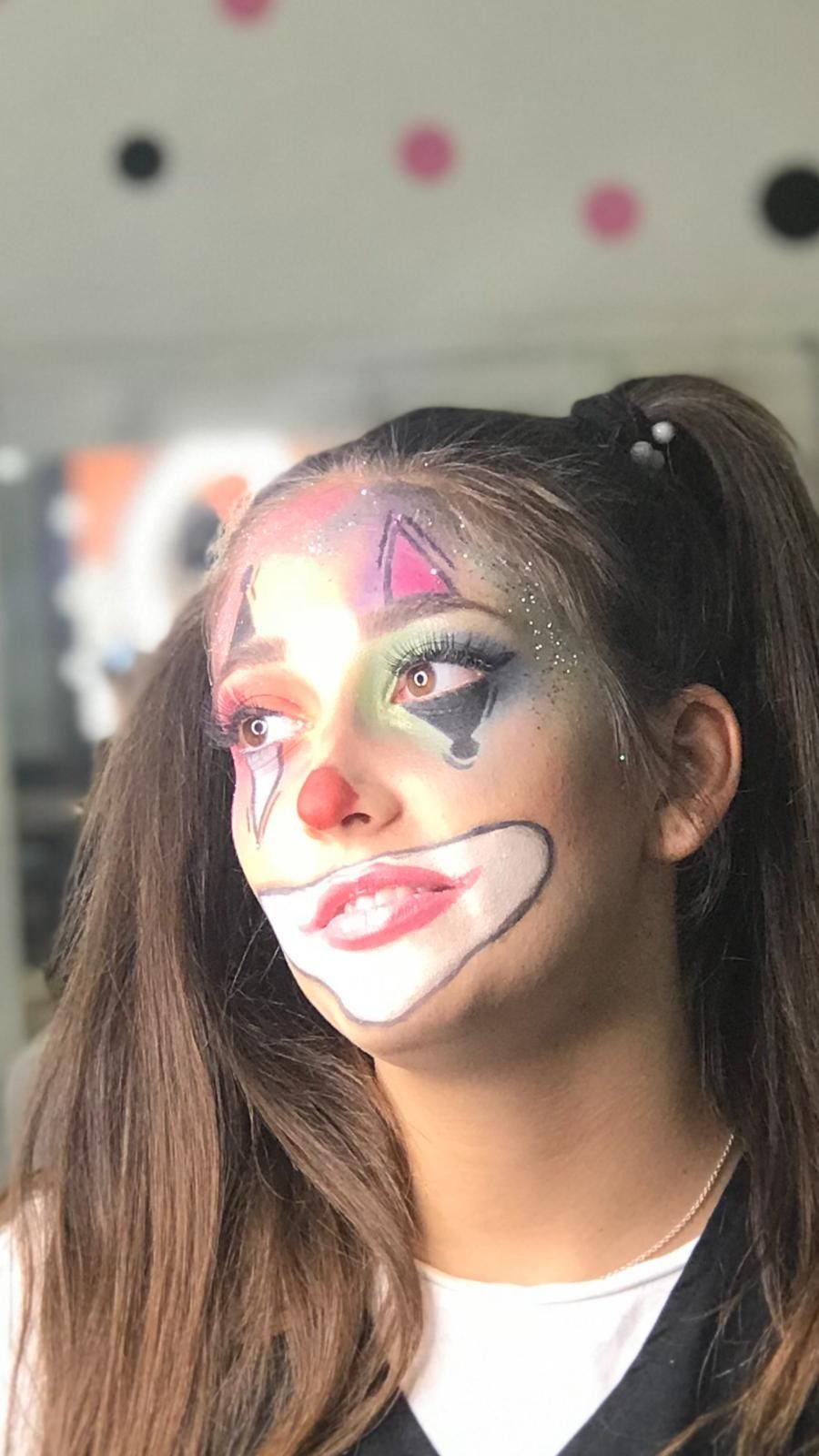 Mujer con maquillaje de payaso, coletas y brillantina. Colores brillantes en la cara, nariz roja y sonrisa.