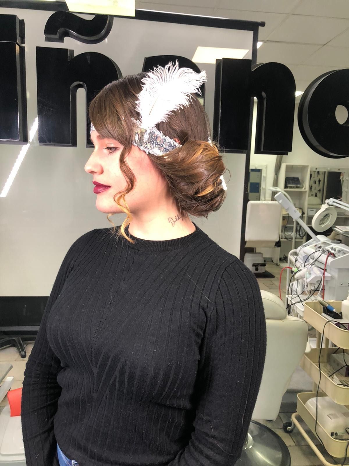 Mujer con cabello oscuro recogido en un moño lateral, con un tocado de plumas blancas y un suéter negro.