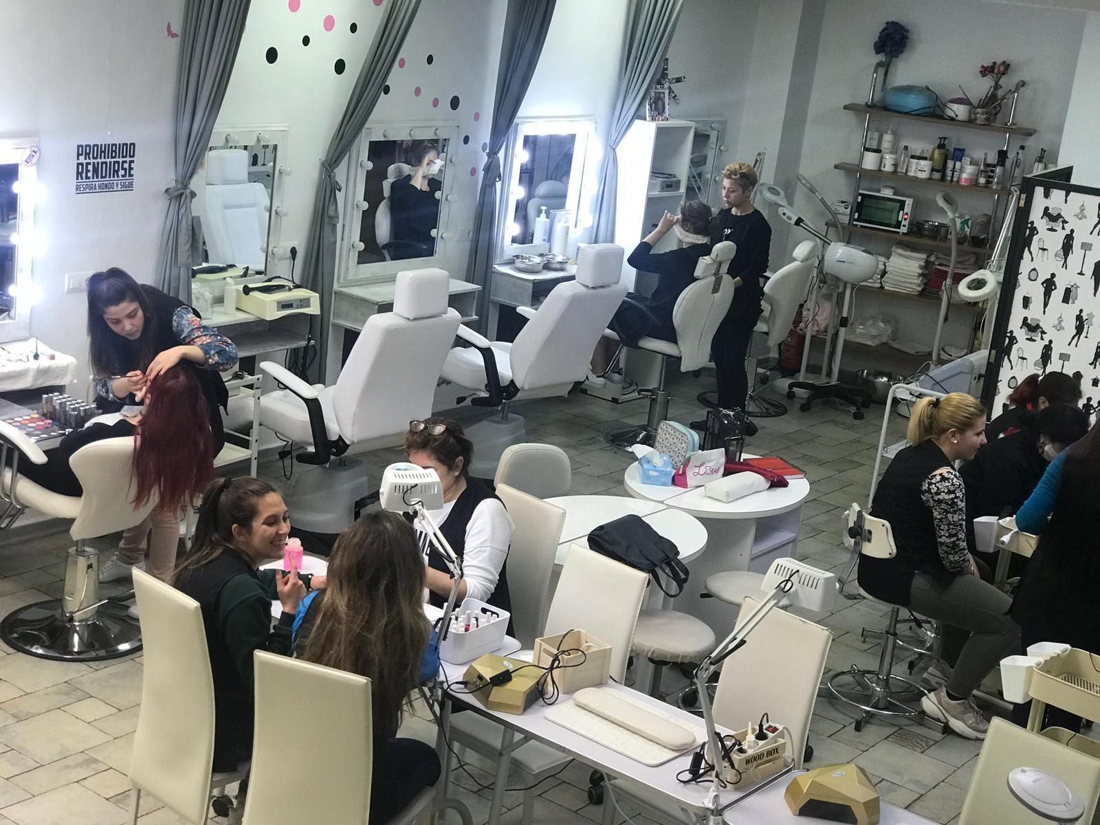 Un salón de belleza con varias mujeres haciéndose maquillaje, manicura y peluquería. Decoración en blanco y negro.