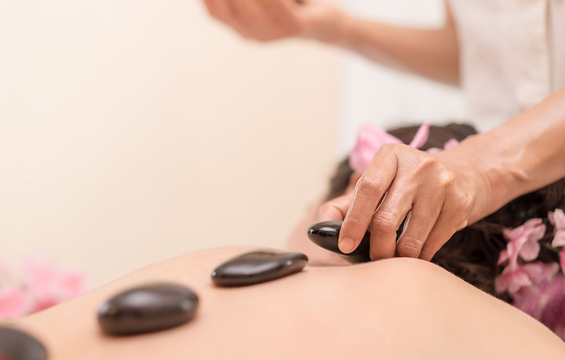 Persona que recibe un masaje con piedras calientes en un spa; el terapeuta le coloca una piedra en la espalda.