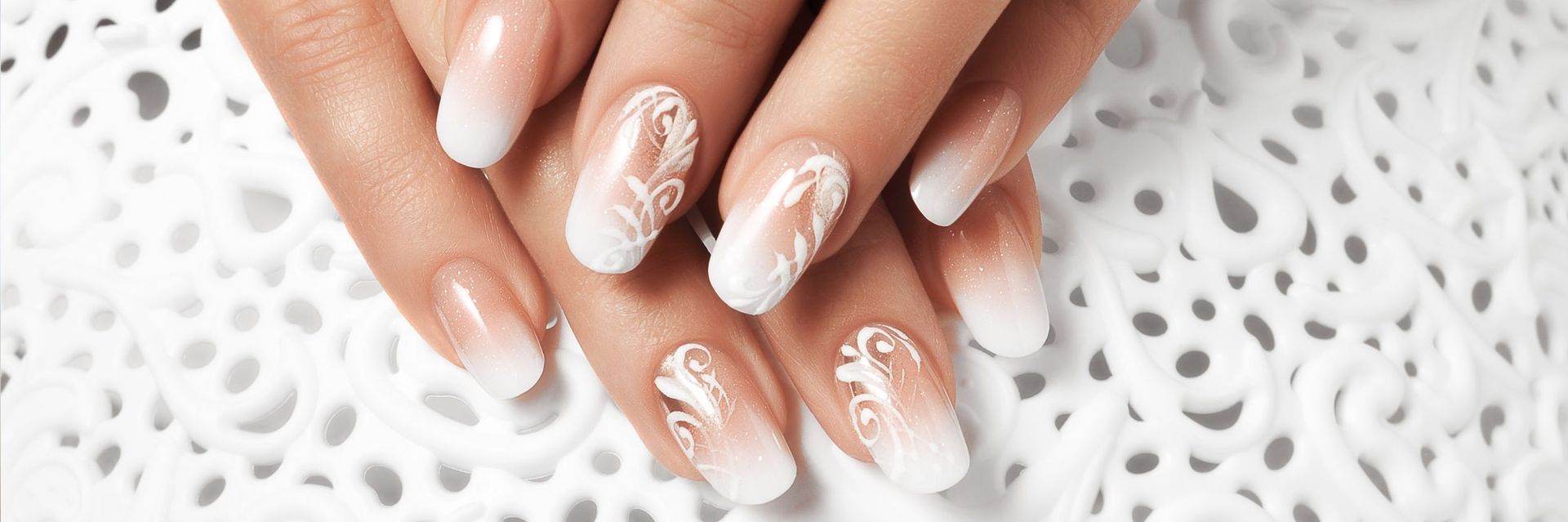 Primer plano de manos con una elegante manicura francesa en tono ombré blanco con acentos florales.