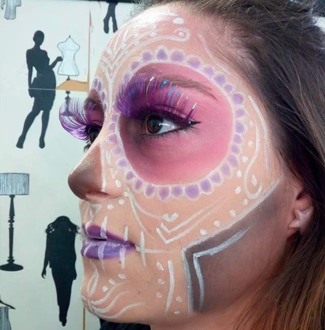 Perfil lateral de mujer con maquillaje del Día de Muertos: pintura rosa, morada, blanca, marrón y negra.