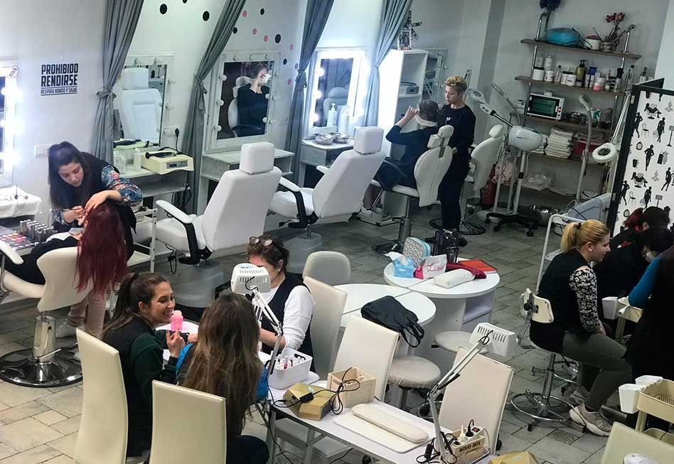 Interior de salón de belleza con varias personas recibiendo tratamientos de belleza.