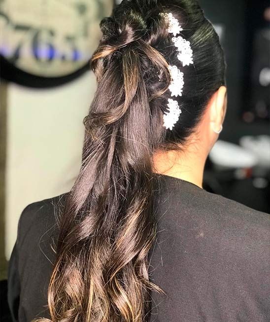 Mujer con cabello oscuro peinado en una cola de caballo rizada y semirecogida, adornada con horquillas con flores blancas.