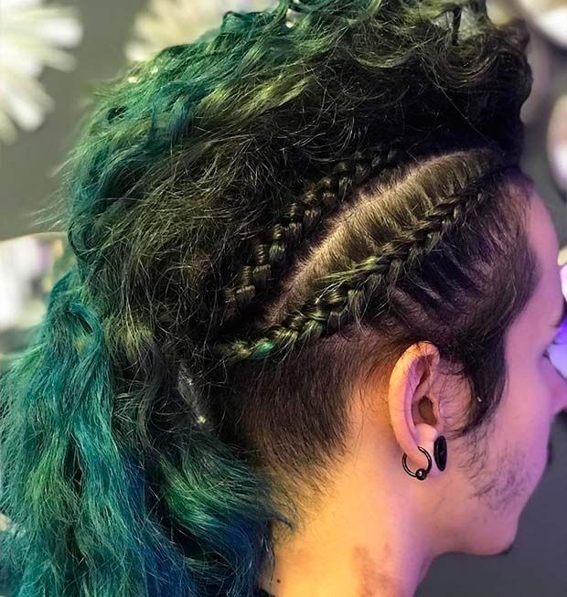 Persona con cabello texturizado con puntas verdes, peinado en un mohawk con trenzas laterales; dilataciones en las orejas.
