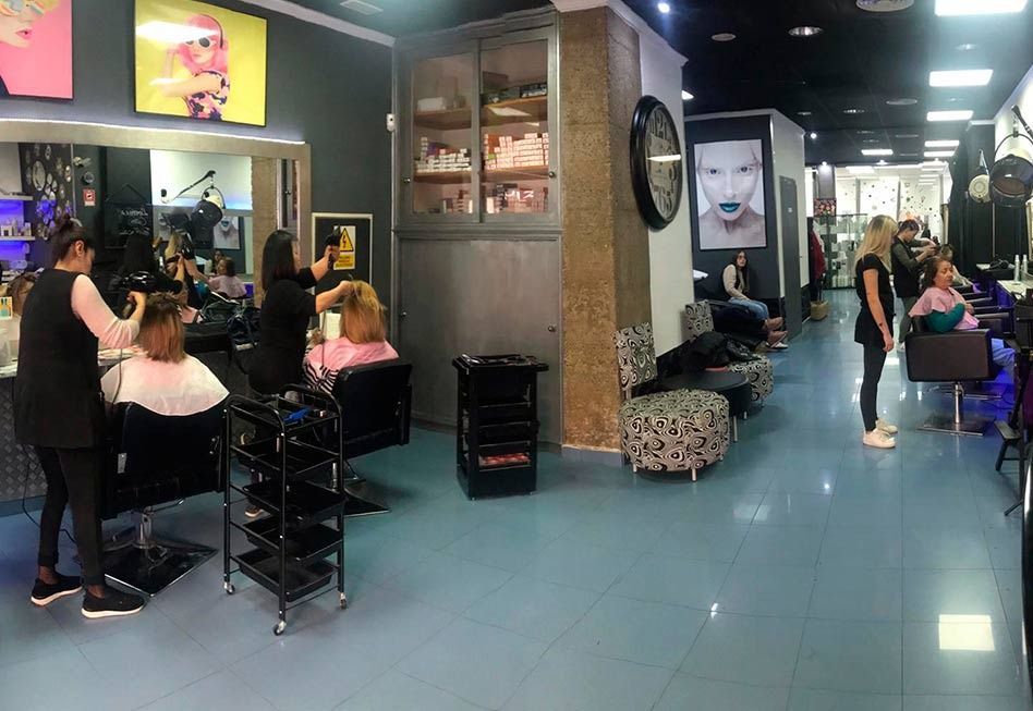 Interior de peluquería con estilistas y clientes cortándose el pelo. Suelo azul, iluminación brillante y decoración.