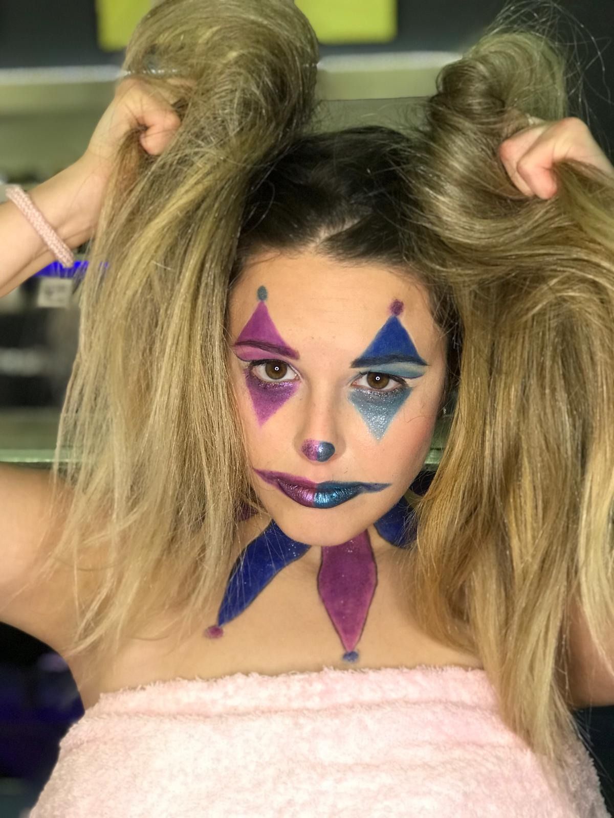 Mujer con maquillaje de payaso, con el pelo recogido en coletas. Maquillaje morado, azul y con brillantina.